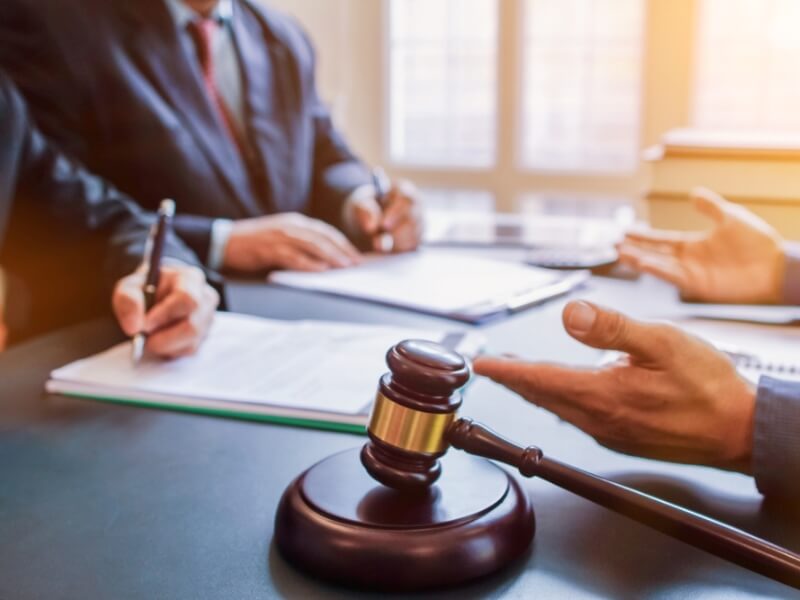 A lawyer stands before a judge in a courtroom engaged in a legal discussion with courtroom decor in the backgroun