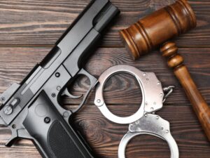 Handgun with metal handcuffs and a wooden gavel on a dark wooden surface, suggesting crime or courtroom imagery