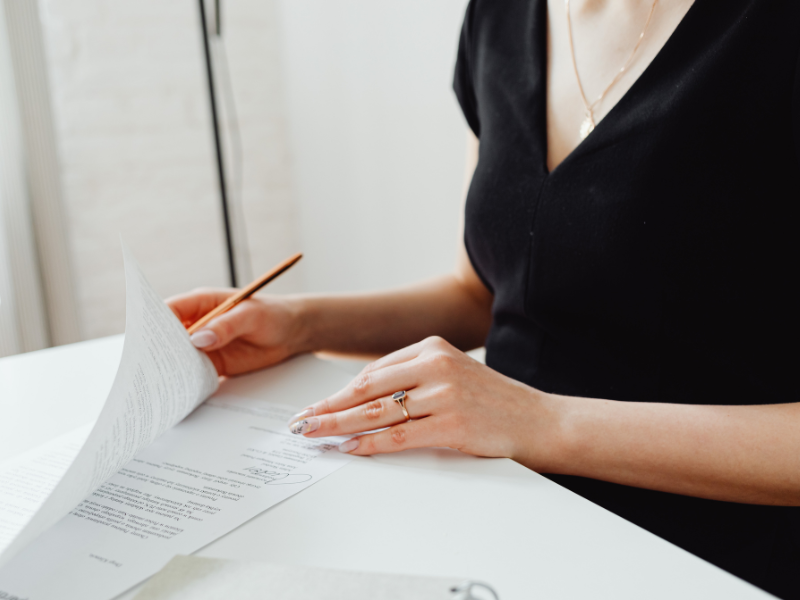 Person in a black top signs a document at a white desk with a pencil nearby.