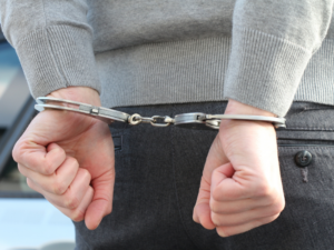 image | ASAP Bail Bonds Houston | ASAP Bail Bonds Houston Person with hands in metal handcuffs behind their back, wearing a gray sweater and dark pants.